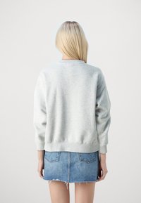 Sudadera gris con cuello redondo y mangas largas, con un ajuste ligeramente holgado. Combinada con una minifalda de denim azul claro.