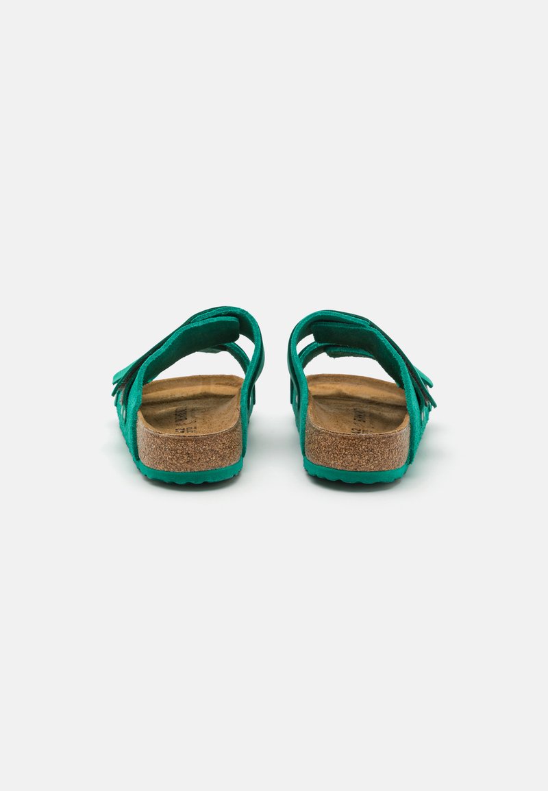 Grüne Wildledersandalen mit doppelten Riemen, Korkfußbett und strukturiertem Gummisohle. Sie verfügen über einen Fransenakzent auf der Rückseite für ein zusätzliches Designelement.