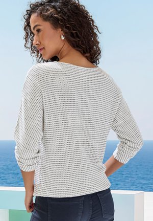 Weißer Pullover mit schwarzen Streifen, in lockerer Passform, mit Dreiviertelärmeln und weicher Textur, kombiniert mit dunkelblauen Jeans.