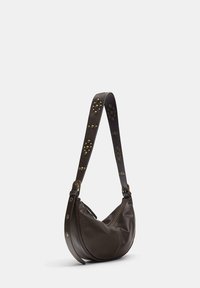 Borsa a spalla in pelle marrone con forma curva. Presenta una tracolla decorata con borchie in ottone e una chiusura con zip. Texture liscia.