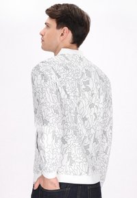 Witte bomberjack met een abstract zwart lijnpatroon, geribbelde manchetten en zoom, met een minimalistisch ontwerp en een gladde textuur.