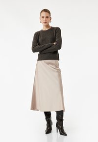 Mørk grå strikket sweater med lange ærmer, parret med en lysebeige satin midi-nederdel. Modellen har sorte højhælede støvler på. Minimal baggrund.