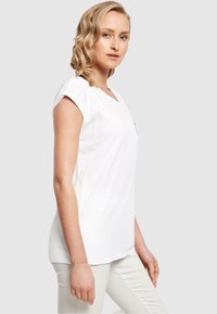 Weißes Baumwoll-T-Shirt mit kurzen, gerollten Ärmeln und V-Ausschnitt. Mit einem kleinen grafischen Detail im linken Brustbereich. Sanfte Textur.