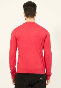 Maglione rosso a maniche lunghe con collo a giro. Realizzato in tessuto morbido, presenta polsini e orlo a coste, con una texture liscia e un design aderente.