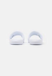 White slide sandals with a thick, textured sole, open back, and cushioned footbed. Smooth surface, minimalistic design, no visible patterns.