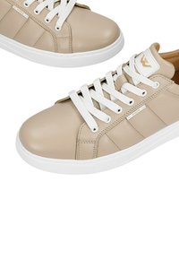 Béžové kožené tenisky s bílými tkaničkami, kulatou špičkou a prošívanými detaily. Mají logo značky na boku a hladký povrch.