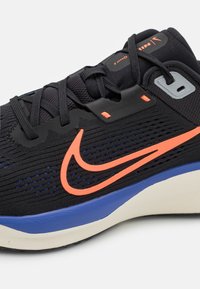 Fekete hálós Nike sportcipő narancssárga és kék dísz�ítéssel. Texturált kialakítással, logóval és támogató gumitalppal rendelkezik.