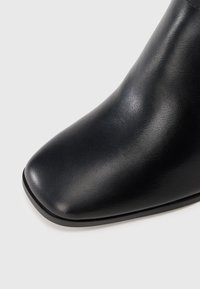 Stivale alla caviglia in pelle nera con una texture liscia, punta affusolata e dettagli di cucitura minimi. La suola presenta una leggera curva sul bordo.