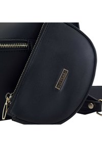 Borsa in finta pelle nera di forma rotonda, con zip e accessori in oro. Include un logo con dettagli dorati sul davanti.