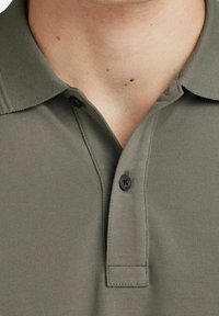 Olijfgroen poloshirt met een gestructureerde stof, een korte kraag en twee zwarte plastic knopen bij de halslijn. Ontworpen voor casual gebruik.
