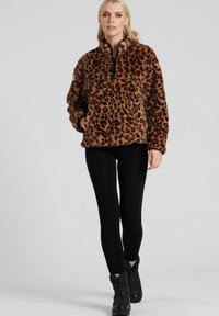 Leopardprint, brun fleece pullover med høj krave, halv lynlås foran og sidelommer, parret med sorte leggings og støvler.