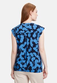 Marinebluse med blåt blomstermønster, korte ærmer, en samlet ryg og glat tekstur, der har en afslappet pasform og rund søm.