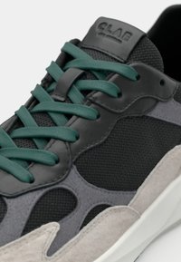 Black and gray sneaker with mesh and suede textures, featuring teal laces and a molded design, highlighted by a white outsole and branding.