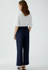 Navy wide-leg pants with a smooth texture and elastic waistband, paired with a white button-up shirt featuring rolled sleeves.