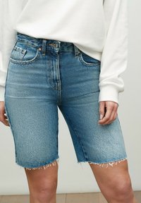 Pantaloni bermuda in denim di colore azzurro chiaro con orlo sfilacciato, presentano una vita alta e cinque tasche, realizzati in tessuto di cotone testurizzato.