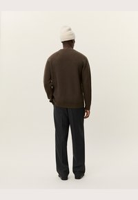 Brun ribbad tröja med avslappnad passform, tillsammans med mörkgrå byxor. Har rund halsringning och långa ärmar. Vit stickad mössa.