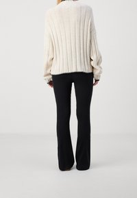 Beige ribbad tröja med överdimensionerade ärmar, med svart kant på fållen och manschetterna, tillsammans med svarta utsvängda byxor.