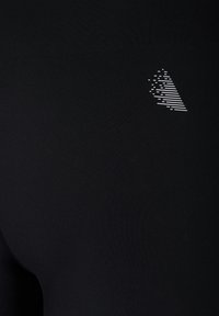 Top sportivo nero realizzato in tessuto liscio ed elastico, con un motivo grafico bianco sulla parte superiore destra composto da linee diagonali e punti.