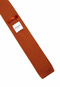 Strikket slips i orange stof med en tekstureret finish. Har et vævet mærke med "JOHN HENRIC" og "SVERIGE." Slankt og rektangulært design.
