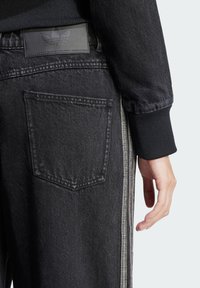 Schwarze Jeans mit geradem Schnitt, ausgestattet mit einer hinteren aufgesetzten Tasche, strukturiertem Denim und hellgrauen Seitestreifen für den Kontrast.