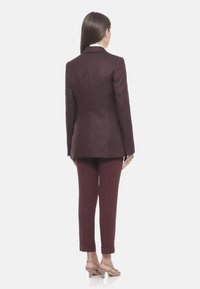 Blazer e pantaloni a righe bordeaux, taglio su misura, texture liscia, design monopetto. Le maniche presentano dettagli con bottoni, gamba slim.