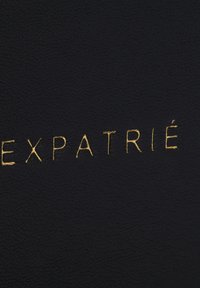 Schwarze, strukturierte Oberfläche mit dem Wort "EXPATRIÉ" in erhabenem, goldenem Schriftzug, der ein modernes, elegantes Design betont.