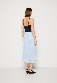 Haut sans manches noir avec bretelles réglables, associé à une jupe midi plissée bleu clair présentant des détails froncés et une texture brillante.