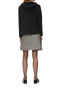 Zwarte hoodie met een kangoeroezak, gecombineerd met een zwart-wit gestreepte rok. Doorzichtige zwarte panty’s en zwarte schoenen maken de look compleet.