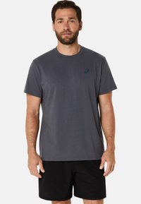 Grå bomulds T-shirt med rund halsudskæring og korte ærmer, prydet med et diskret blåt logo på brystet; parret med sorte shorts.