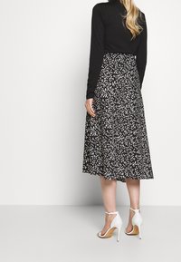 Svart kjol i medellängd med ett vitt spräckligt mönster, ihop med en figurnära svart långärmad topp och vita klacksandaler.