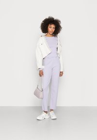 Top listrado em lavanda e calças a condizer com uma borda desfiada, sobrepostas com uma jaqueta de ganga branca cropped. Complementado por uma pequena mala rosa e ténis brancos.