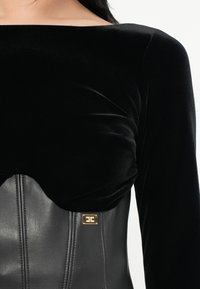 Black velvet long-sleeve top with a fitted leather bodice, featuring a smooth texture and a gold hardware accent at the waist.