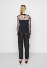 Marinblus med genomskinliga, prickiga långärmar och nyckelhålsdetalj i ryggen, tillsammans med svarta läderbyxor och klackar med remmar.