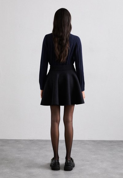 Jersey de punto acanalado color navy combinado con una falda negra de corte acampanado, medias traslúcidas y zapatos negros gruesos, visto desde la parte de atrás.