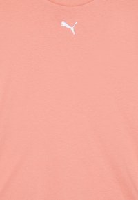 Camiseta de color coral claro en algodón suave con cuello redondo. Presenta un pequeño logotipo de PUMA en blanco bordado en el pecho. Textura suave.