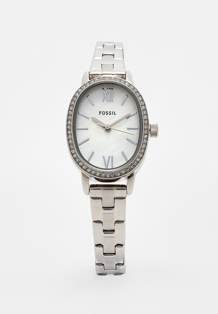 Reloj ovalado de plata con esfera de nácar, números romanos y un bisel adornado con cristales. Presenta una pulsera metálica enlazada.