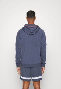 Hoodie bleu marine avec un accent rouge sur la capuche, doté d'une coupe décontractée et de poignets côtelés, assorti à un short assorti avec un design simple.