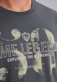 Camiseta de algodón gris con gran texto blanco y patrones circulares abstractos, con un logo mostrado de manera destacada cerca del escote.