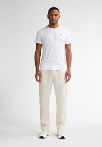 Hvid bomulds t-shirt med rund hals og lille broderet logo, parret med lyse beige linnedbukser og hvide sneakers.