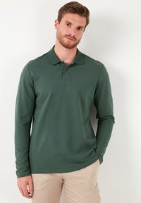 Camisa polo de manga larga en verde oscuro, hecha de una suave tela de algodón, con un cuello clásico y una tapeta de tres botones.