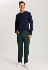 Marineblauwe henley-shirt met lange mouwen en drie knopen, gecombineerd met donkergroene joggingbroek met een trekkoord en zijstrepen, gedragen met witte sneakers.