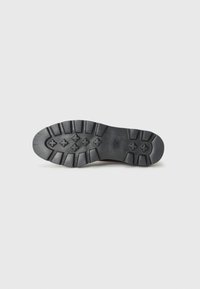 Semelle de chaussure en caoutchouc noir avec une surface texturée, dotée d'un motif de crampons multidirectionnels et de sections renforcées pour une meilleure adhérence.
