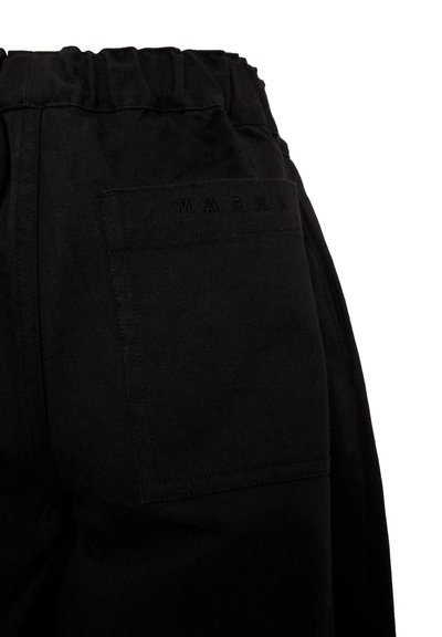Pantalons en coton noir avec une taille élastique et une poche arrière simple portant un logo en relief. Le tissu a une texture lisse.