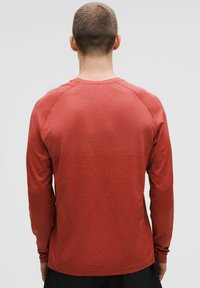 Cămașă cu mâneci lungi dintr-un material texturat roșu. Are guler rotund și mâneci raglan. Finisaj neted cu un model subtil.