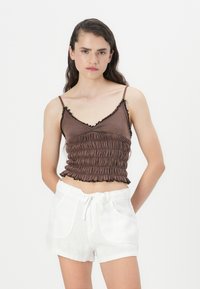 Brun bomull crop top med volanger og samlet tekstur, parret med hvite linshorts med drakordliv og lommer.