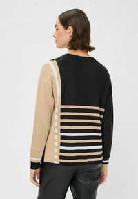 Strickpullover mit einer Mischung aus beige- und schwarzfarbigen Paneelen, verziert mit weißen Streifen und Akzenten. Rundhalsausschnitt und lange Ärmel.