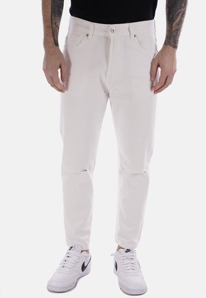 Jeans in denim bianco con una vestibilità slim, aree strappate sulle ginocchia e chiusura classica con bottone. Indossati con sneakers bianche per un contrasto.