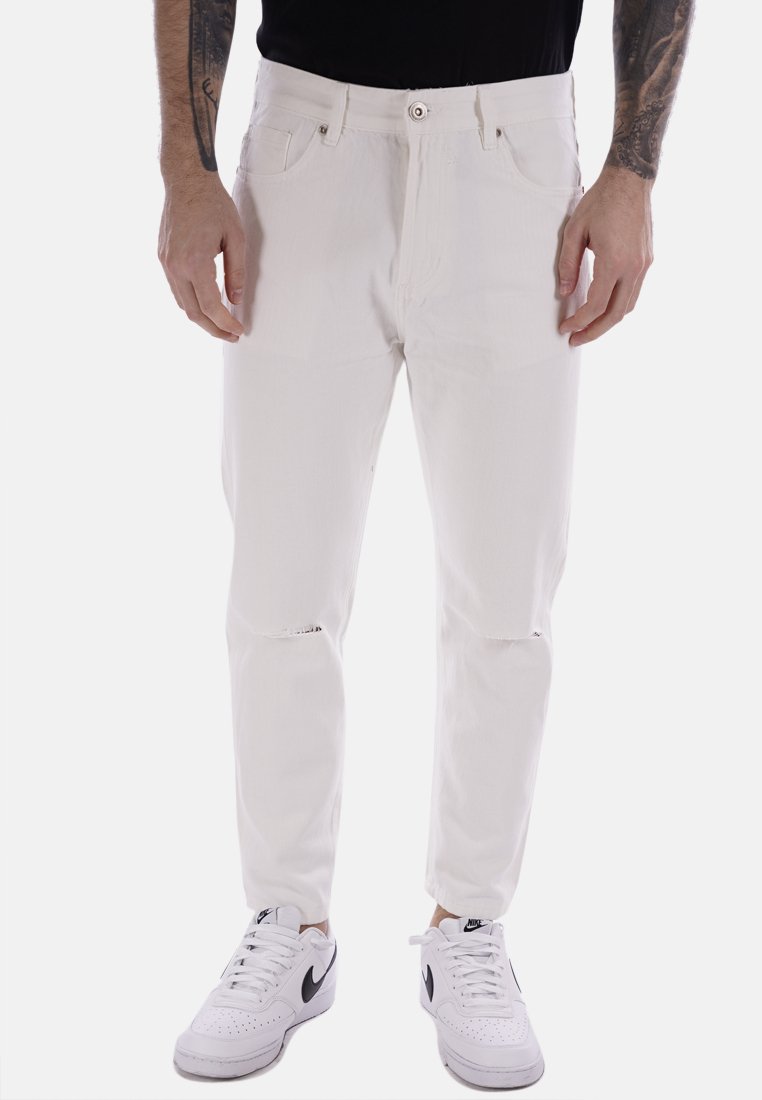 Jeans in denim bianco con una vestibilità slim, aree strappate sulle ginocchia e chiusura classica con bottone. Indossati con sneakers bianche per un contrasto.