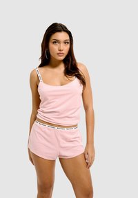 Débardeur rose à côtes avec des fines bretelles et un short assorti, comportant une ceinture de marque. Le matériau semble doux et confortable.