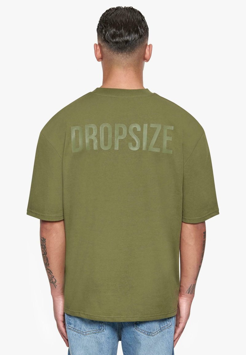 Olivengrünes, oversized T-Shirt mit kurzen Ärmeln und Rundhalsausschnitt. Text "DROPSIZE" hinten in einer tonalen, leicht reflektierenden Ausführung bedruckt.
